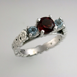 14kt white gold sculpted floral engagement ring set with a 5mm ruby and two 3mm side aquamarine.